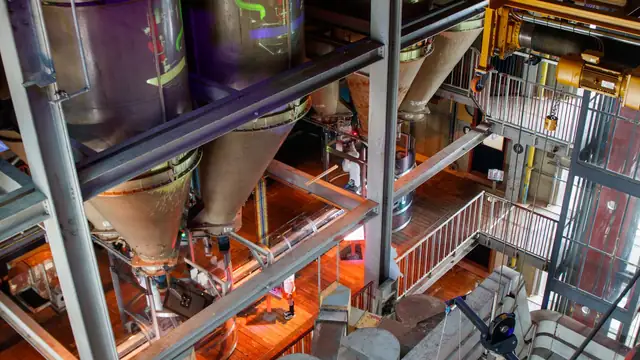 Vista de cima de silos industriais dentro de uma fábrica, com tubulações e equipamentos de processamento