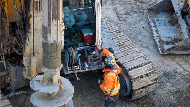 Operário com roupa de alta visibilidade opera equipamento pesado de perfuração em canteiro de obras
