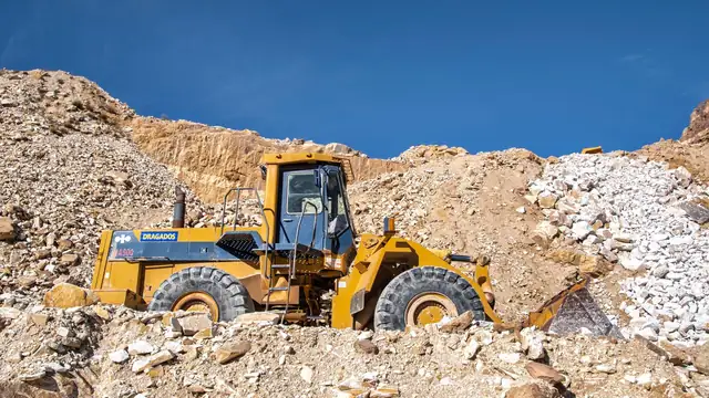 Trator de esteira industrial trabalhando em pedreira ensolarada de terreno rochoso