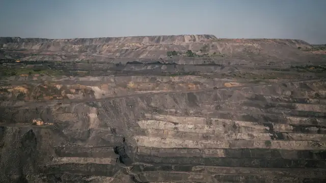 Grande mina a céu aberto sob céu azul, com formações rochosas e paisagem industrial