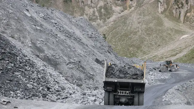 Pedreira com caminhões e máquinas em operação, cercada por terreno montanhoso e acidentado