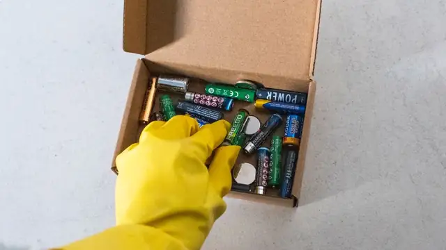 Mão com luva de proteção manuseando baterias usadas para reciclagem