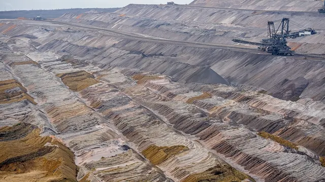 Vista aérea de cava de mineração a céu aberto com maquinário e camadas de solo expostas