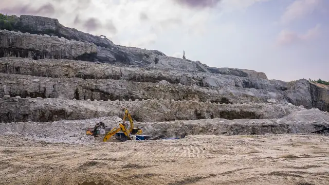 Pedreira com escavadeiras trabalhando em terreno rochoso sob céu nublado