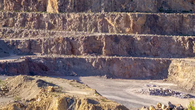 Vista ensolarada de pedreira com camadas de rocha expostas e terreno rochoso