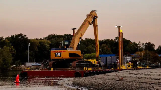 Escavadeira instalada sobre uma balsa na água, ao entardecer