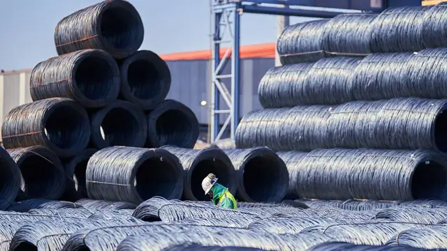 Trabalhador com equipamento de proteção inspeciona bobinas de aço empilhadas em área industrial