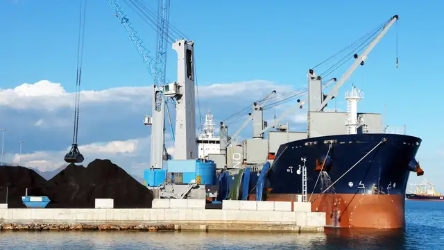 Navio de carga e guindastes em porto industrial, durante o carregamento de minerais sob céu azul