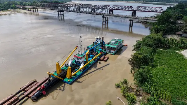 Balsa de dragagem operando em um rio, com ponte ao fundo