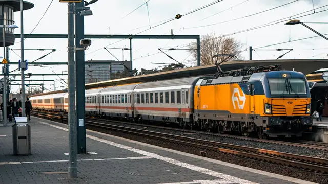 Locomotiva moderna parada em estação ferroviária, com composição de passageiros ao lado da plataforma