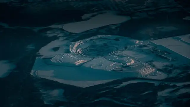 Vista aérea de degraus rochosos de uma mina a céu aberto coberta de neve, em área industrial, ao entardecer