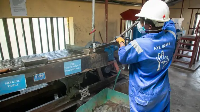 Operário de macacão azul opera uma mesa vibratória usada no processamento de minério