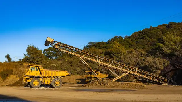 Caminhões basculantes amarelos e correia transportadora em área de mineração