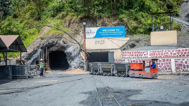 Entrada de túnel de mina com vagonetes sobre trilhos e trabalhadores com equipamento de segurança