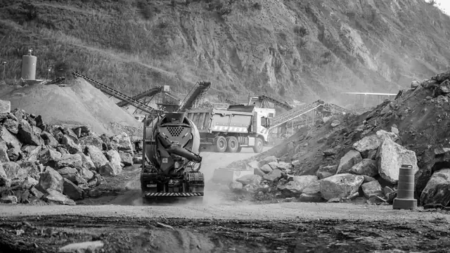 Imagem em preto e branco de caminhões e máquinas em uma pedreira de terreno acidentado