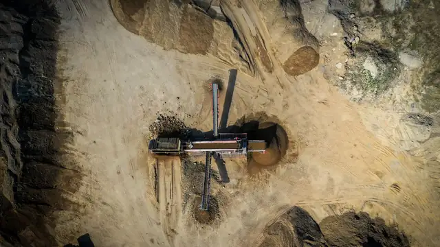 Vista aérea de terreno de relevo ondulado com marcas de escavação e atividade de extração mineral à luz do dia