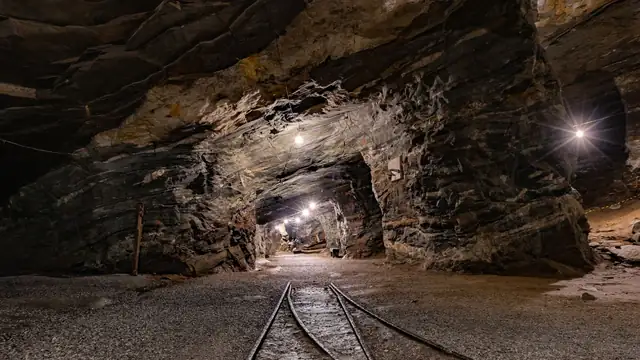 Túnel subterrâneo de mina iluminado, com paredes de rocha e luzes ao longo do trajeto