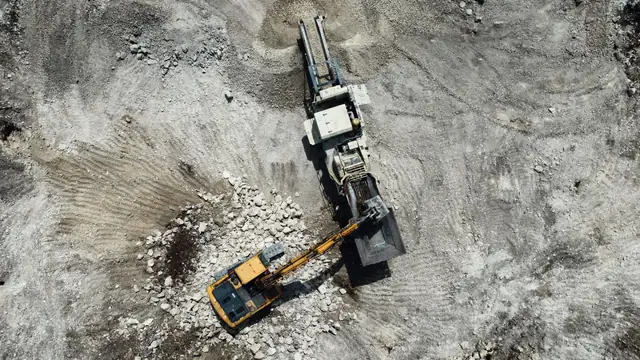 Vista aérea de escavadeira e máquinas em uma pedreira, com atividade de mineração e construção