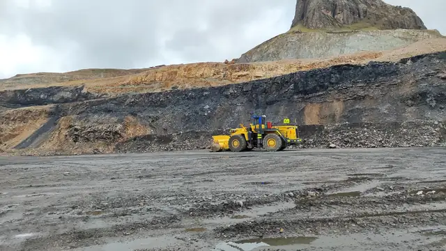 Carregadeira amarela trabalhando em área de pedreira de relevo acidentado