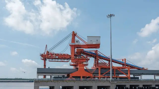 Guindaste industrial laranja em um porto à beira da água, sob céu azul