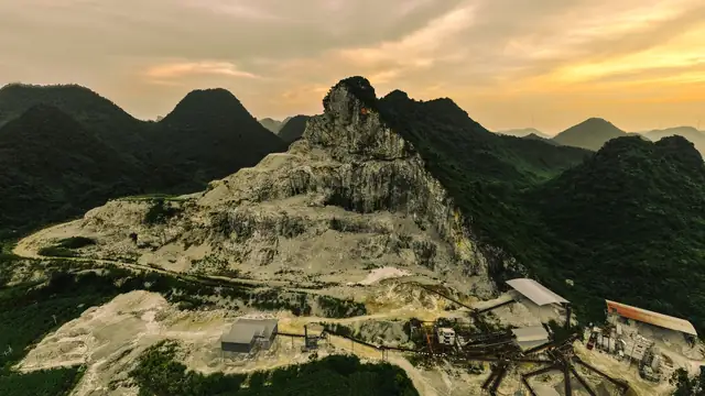 Vista aérea de uma pedreira cercada por montanhas verdes ao pôr do sol
