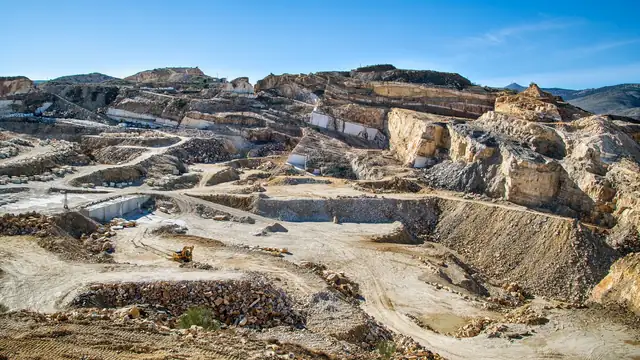 Vista ampla de uma grande cava a céu aberto, com camadas de rocha e máquinas pesadas em operação