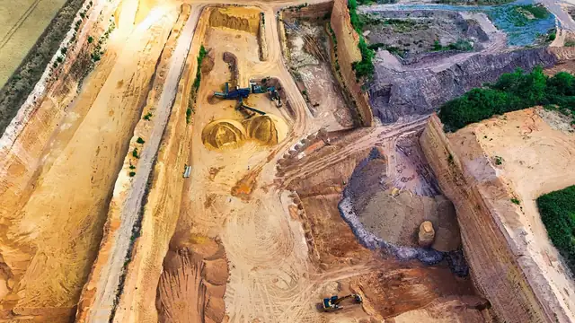 Vista aérea de grande pedreira de arenito com maquinário pesado escavando e pilhas de areia