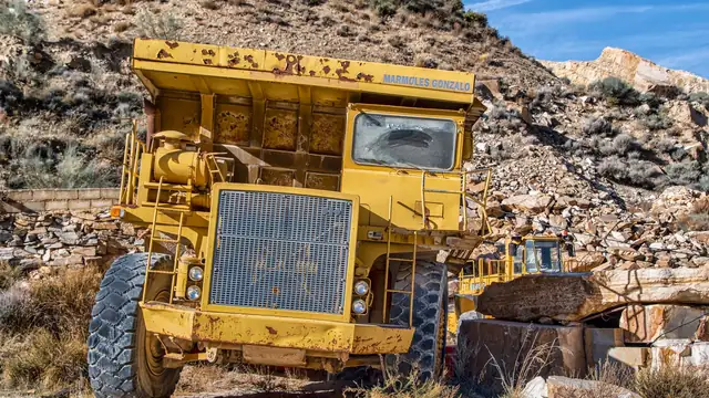 Caminhão de mineração parado em pedreira rochosa e árida, sob céu azul