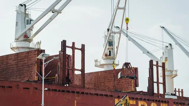 Navio de carga atracado em porto industrial com guindastes realizando descarga