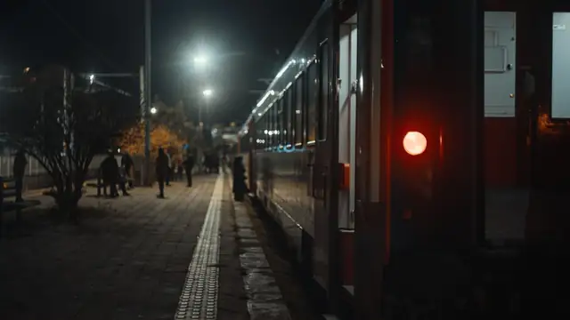 Plataforma ferroviária com iluminação fraca à noite, com um trem parado e passageiros ao lado