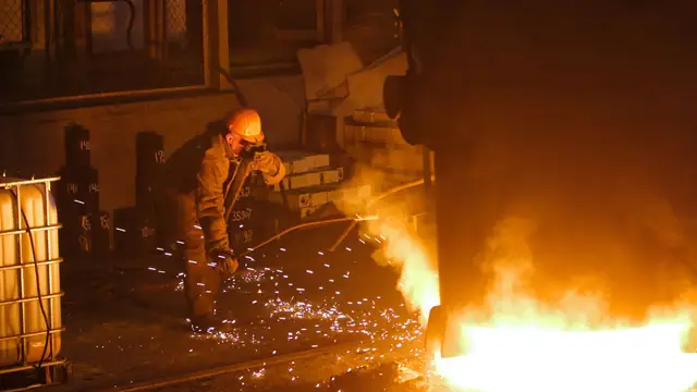 Trabalhador de siderúrgica em equipamento de proteção solda peças de metal perto de metal fundido
