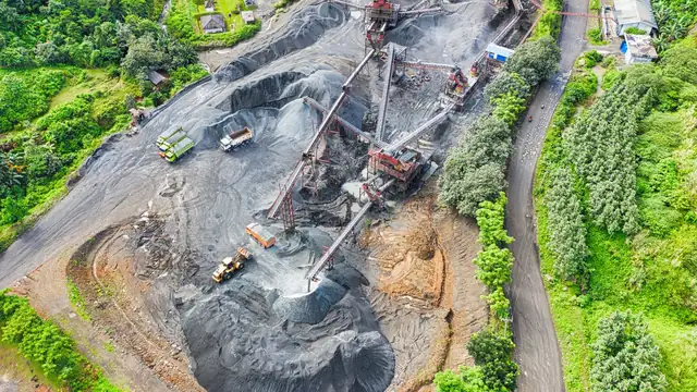 Vista aérea de área de mineração cercada de mata, com pilhas de material e correias transportadoras