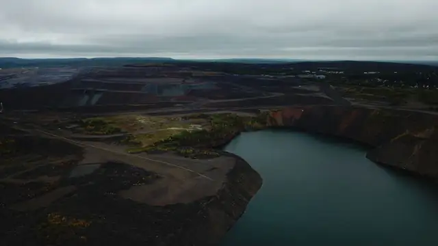 Vista aérea de um lago formado em área de mina e da paisagem ao redor, em dia nublado